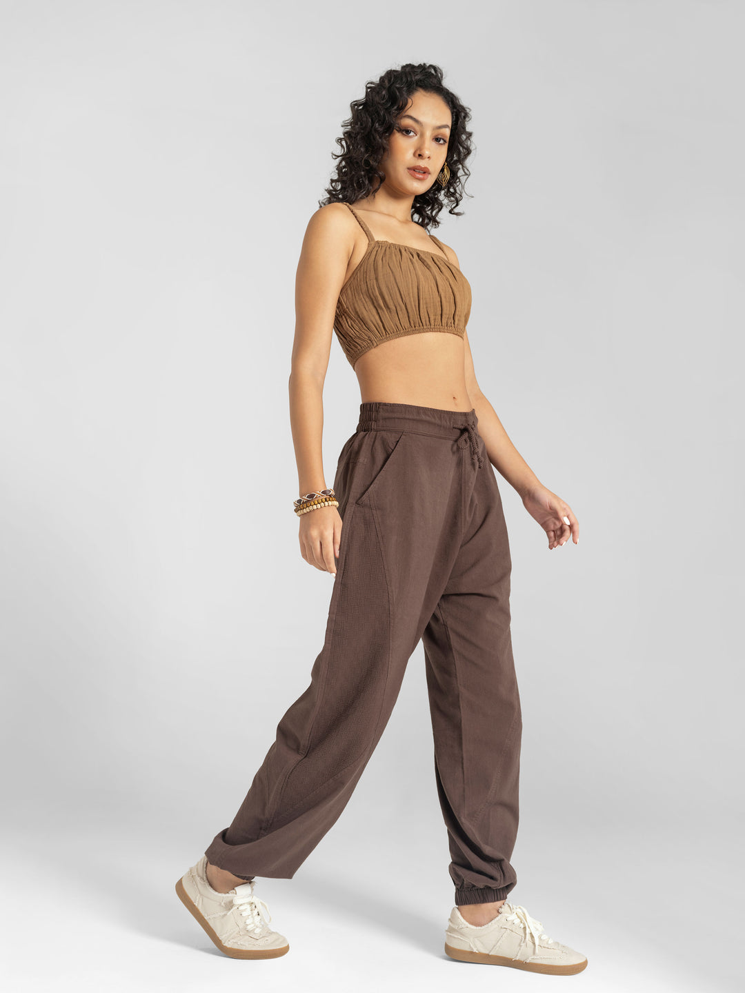 Woman wearing a brown crop top and high-waisted pants on a white background